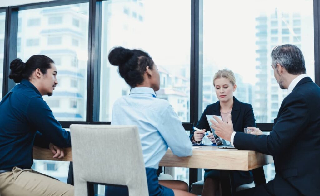 A group of corporate people at desk in the office discussing.